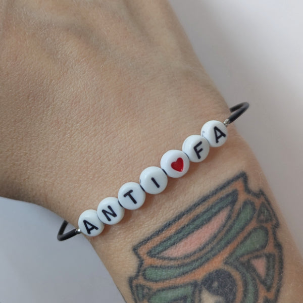 Vegan und handgemacht Armband: ANTIFA mit rotem Herz, bestehend aus wasserfestem Kunstlederband mit Kunststoffperlen und rostfreiem Edelstahl, passend zur rebellischen RUDE REBEL Kollektion.