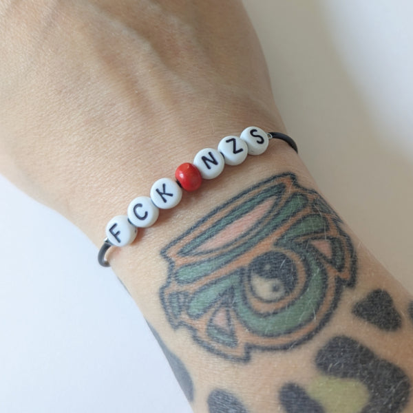Vegan und handgemachtes Armband: FCK NZS mit roter Perle, aus wasserfestem Kunstleder und Edelstahl, perfekt für einen rebellischen, nachhaltigen Stil.