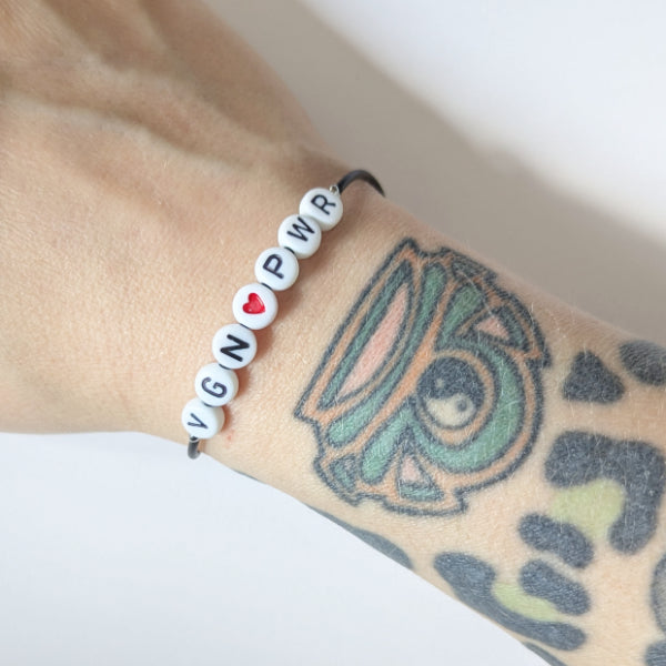 Handgemachtes Armband VEGAN POWER mit Kunstlederband und Kunststoffperlen, verziert mit rotem Herz-Anhänger, wasserfest und aus Edelstahl, von RUDE REBEL.