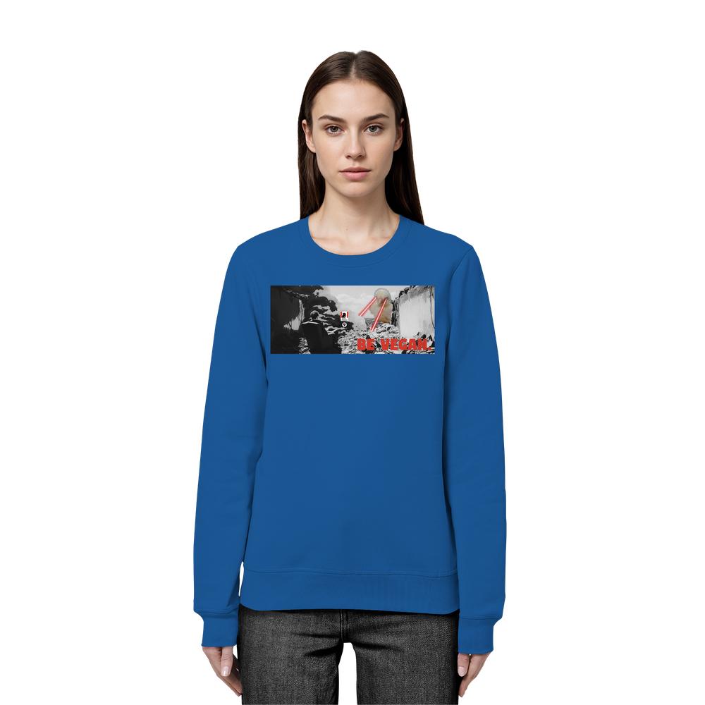 Frau trägt blaues Vegan und Bio Sweatshirt: BE VEGAN, mit stilisiertem Landschaftsmotiv, Löffel, Essstäbchen und rotem Schriftzug, aus Bio-Baumwolle und recyceltem Polyester.