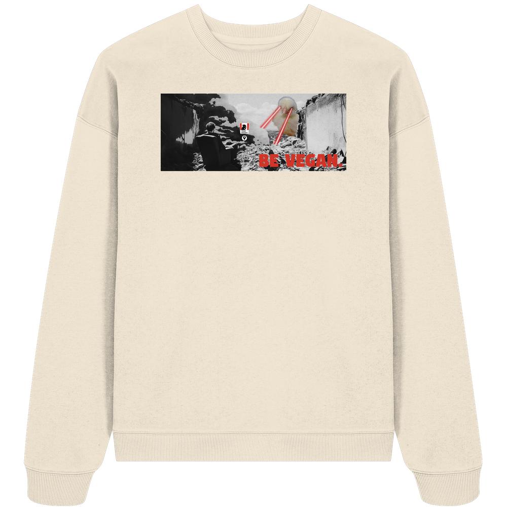 Vegan und Bio Oversized Sweatshirt: BE VEGAN. - Angry bird, zeigt apokalyptisches Stadtmotiv mit Sessel, Trümmern und rotem Laserauge. 100% Bio-Baumwolle, rebellisches veganes Design.